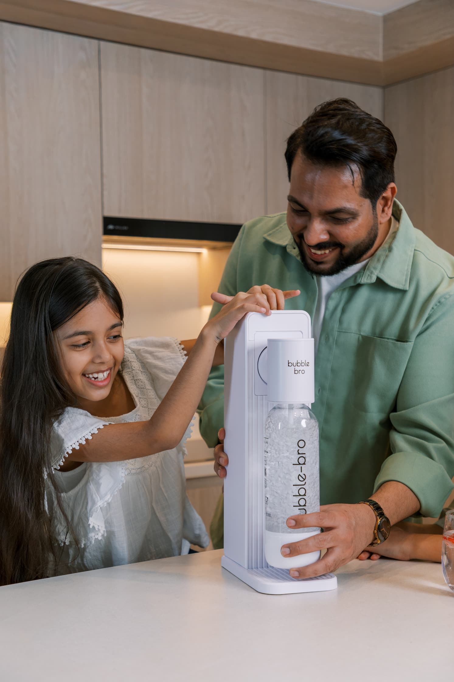 Father and daughter making fresh sparkling water at home with the bubble-bro Origin in white on a modern kitchen counter