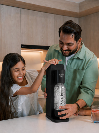 Father and daughter carbonating fresh sparkling water with the bubble-bro Origin in black at home in their modern kitchen 
