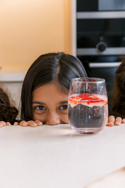 Young girl admiring a glass of fresh strawberry sparkling water made at home with the bubble-bro Origin — kid-friendly fizzy drink 