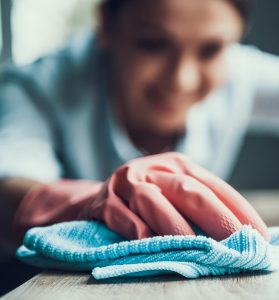 Young Smiling Woman in Gloves Cleaning House. Closeup of Happy Beautiful Girl wearing Protective Gloves Cleaning Desk by spraying Cleaning Products and wiping with Sponge. Woman Cleaning Apartment